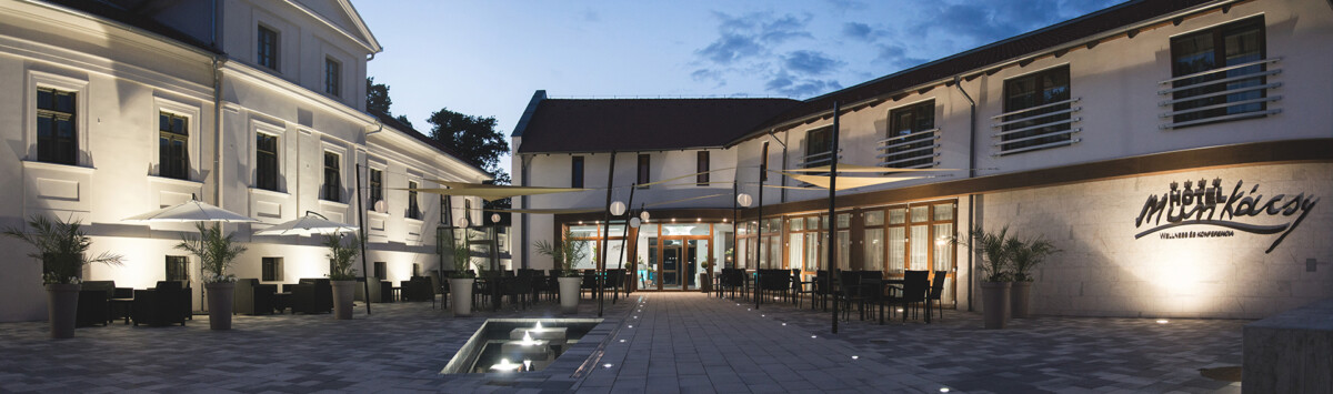 Nighttime view of the Munkácsy Hotel's outdoor area, showcasing a contemporary design with a tranquil water feature, patio seating, and a well-lit entrance